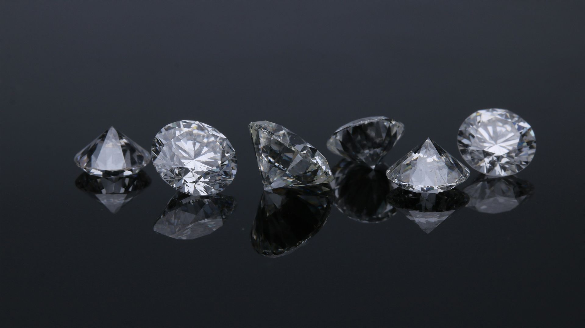Six faceted diamonds arranged in a row on a reflective black surface